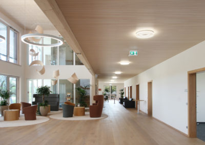 Foyer von Holzbau Aumann, Deckneleuchten im Flur mit Lichtkorona, Luftraum mit großen Lichtringen, Blick auf die Lounge